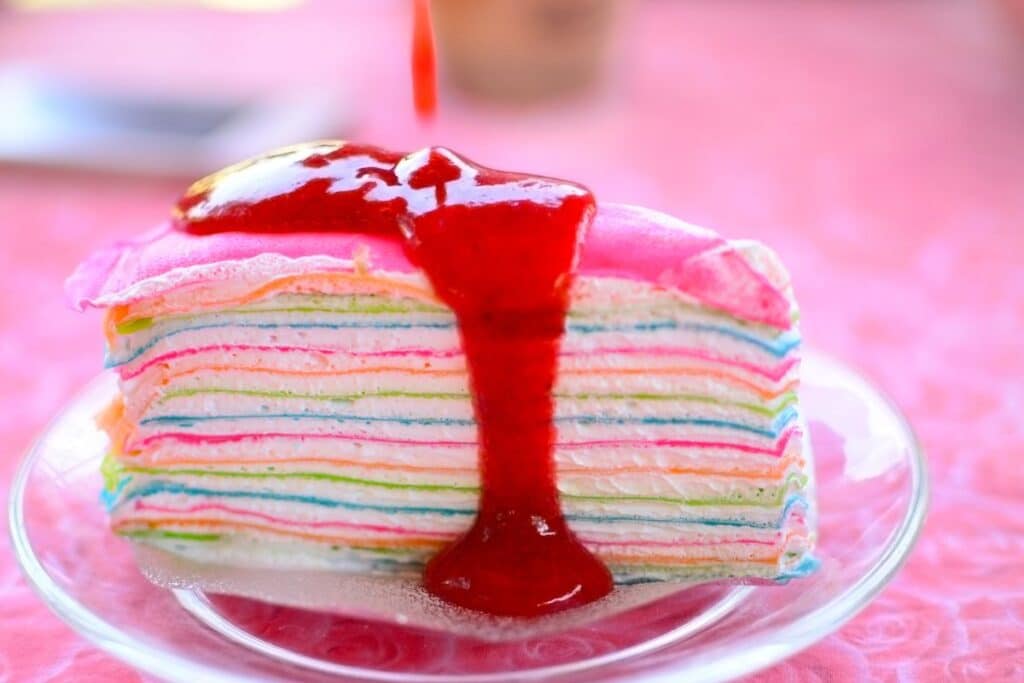 Gâteau crêpes arc-en-ciel avec coulis rouge.