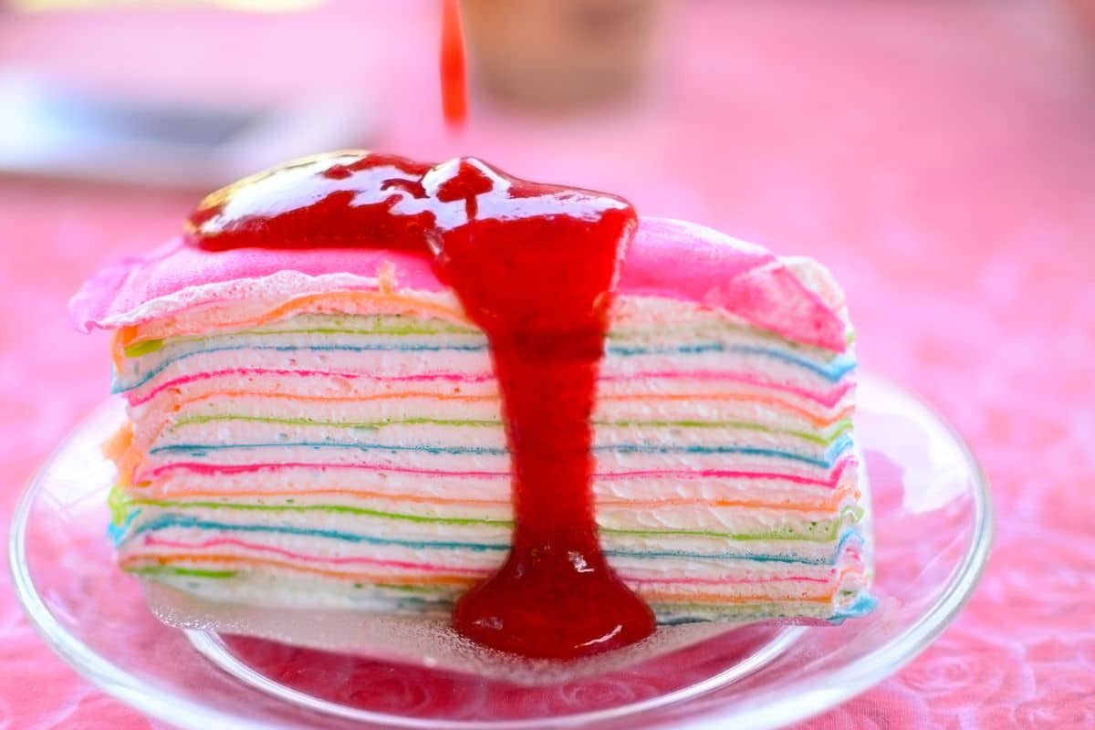 Gâteau crêpes arc-en-ciel avec coulis rouge.