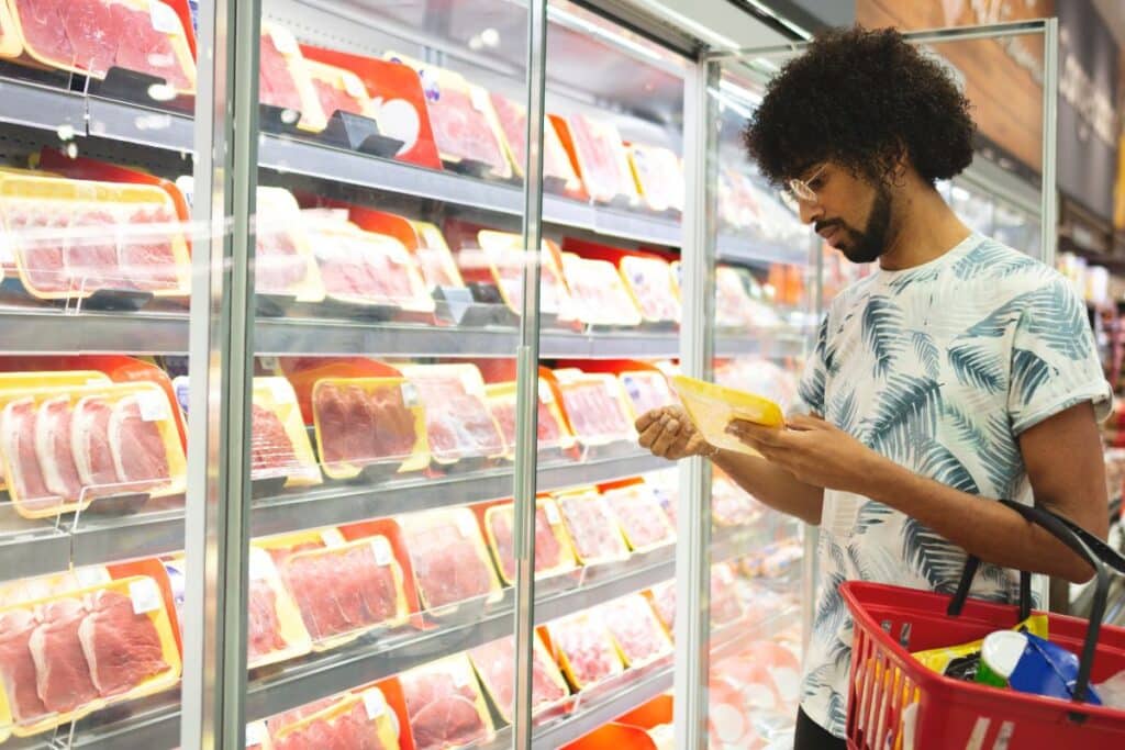 Acheteur examine des paquets de viande en supermarché.