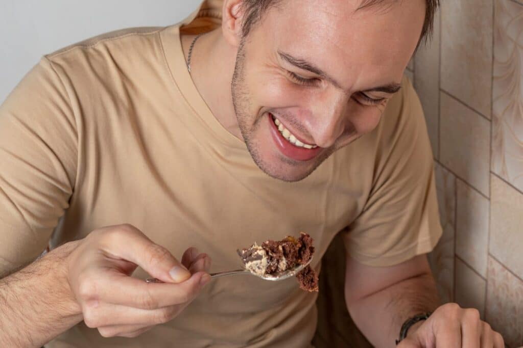 Homme souriant mange du gâteau avec une cuillère.