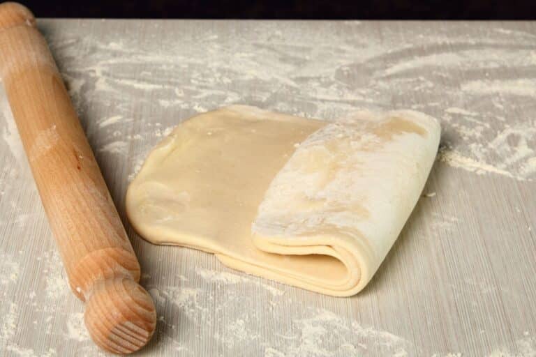 Pâte feuilletée et rouleau à pâtisserie sur table.
