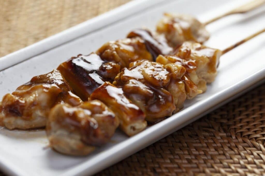 Brochettes de poulet sauce teriyaki sur assiette blanche.