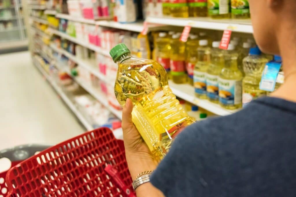 Personne tenant une bouteille d'huile au supermarché.
