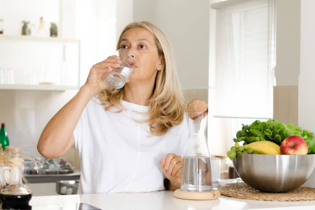 Femme buvant de l'eau dans une cuisine lumineuse.