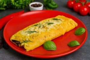 Omelette au fromage garnie d'herbes sur assiette rouge.