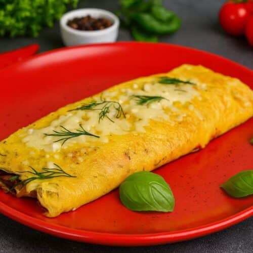 Omelette au fromage garnie d'herbes sur assiette rouge.