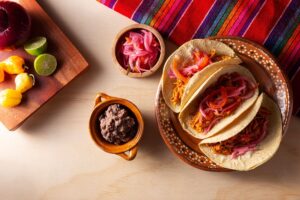 Tacos mexicains, garnitures et condiments sur table colorée.