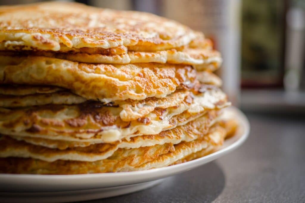 Pile de crêpes dorées sur assiette blanche.