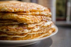 Pile de crêpes dorées sur assiette blanche.