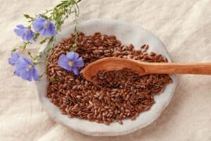 Graines de lin avec fleurs violettes et cuillère bois.