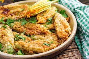 Fleurs de courgette farcies et frites dans une assiette.