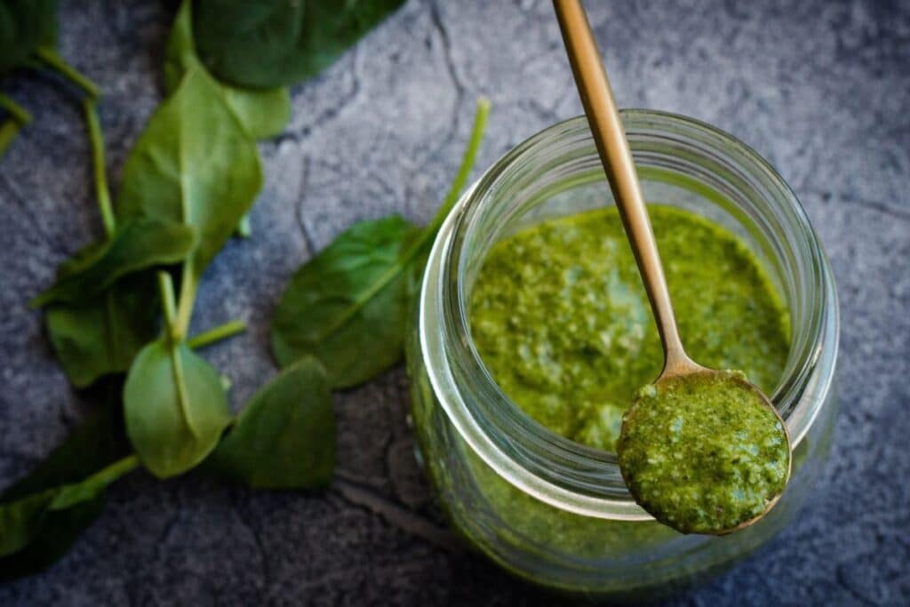 Pot de pesto avec cuillère et feuilles.