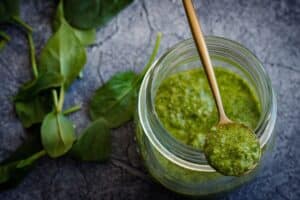 Pot de pesto avec cuillère et feuilles.
