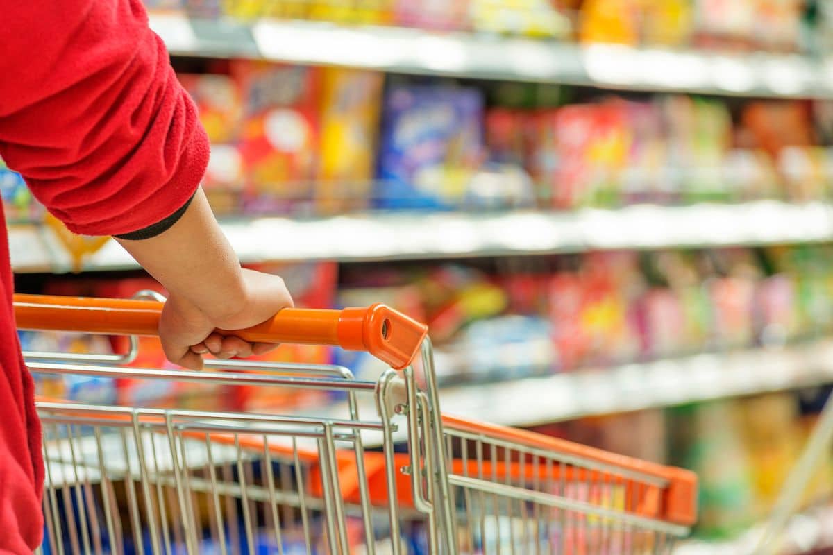Personne poussant un chariot dans un supermarché coloré.