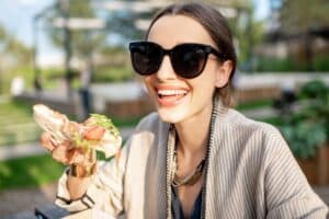 Femme souriante mange un sandwich dehors.