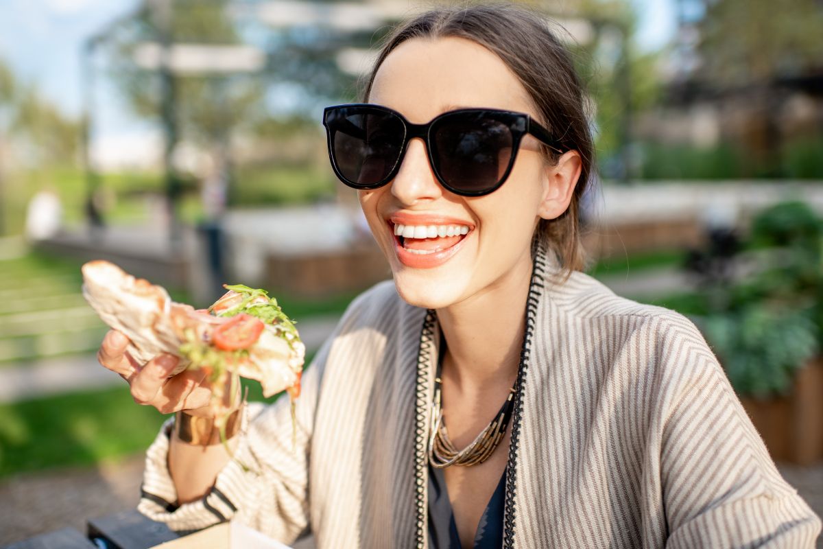 Femme souriante mange un sandwich dehors.