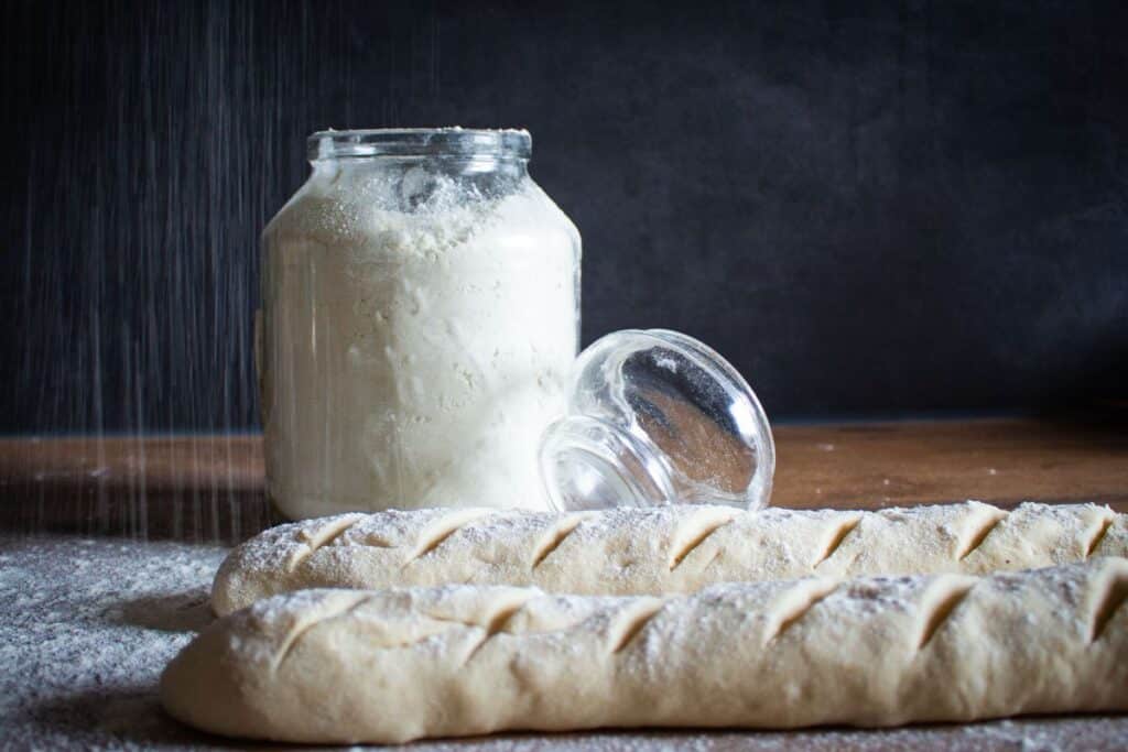 Baguettes crues et pot de farine sur table.