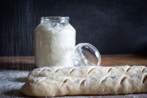 Baguettes crues et pot de farine sur table.