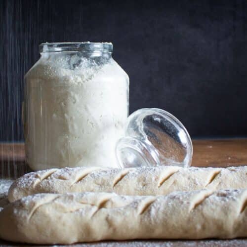 Baguettes crues et pot de farine sur table.