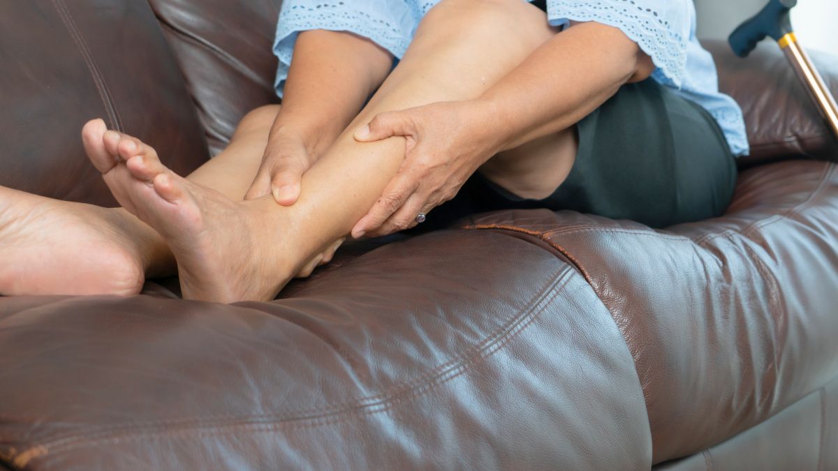 Personne massant sa jambe sur un canapé.