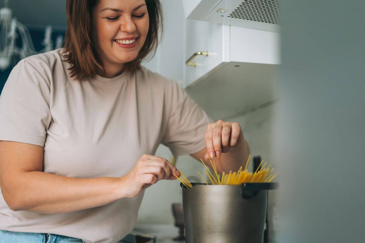 Femme souriante cuisinant des pâtes dans la cuisine.