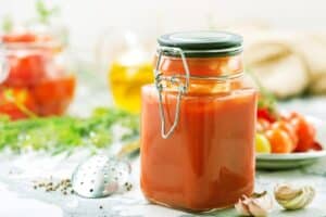Bocal de sauce tomate maison sur table avec herbes.