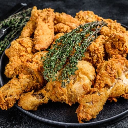 Poulet frit garni de thym sur assiette noire.