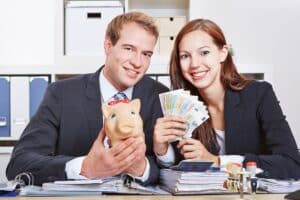 Deux personnes sourient avec tirelire et billets.