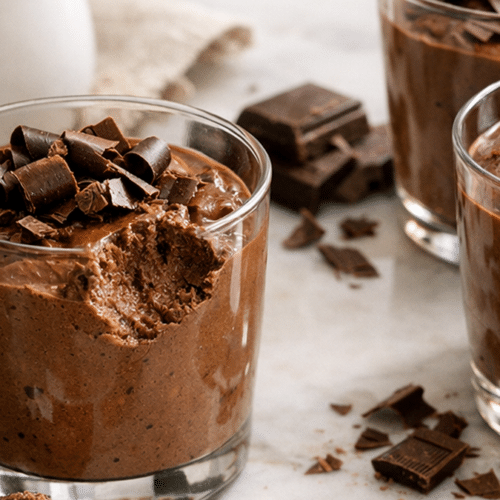 Verrines de mousse au chocolat noir à la texture ferme et fondante, servies avec quelques copeaux de chocolat sur une table claire.