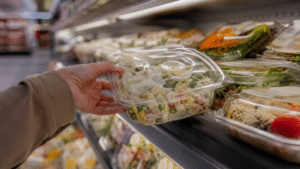 Barquettes de salades traiteur dans un rayon frais de supermarché avec une main qui en prend une